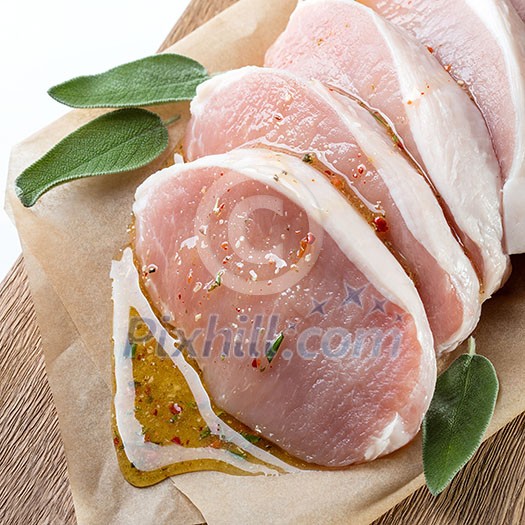 Raw meat. Pork escalope with sause made of honey and herbs with green sage leaves on wooden board against white background. Top view