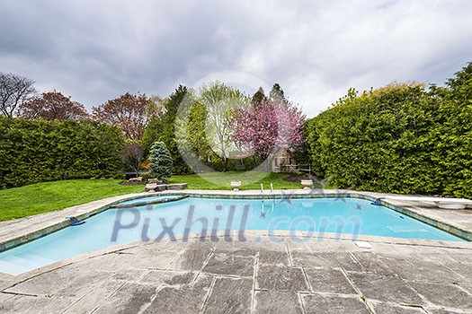 Backyard of residential house in spring with large pool and paved patio Backyard of residential house in spring with large pool and paved patio