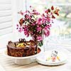 Round gourmet chocolate cake on table next to window with plates, cutlery, and pink spring bouquet