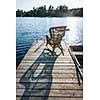 Wicker rocking chair on wooden dock in summer at small lake casting long shadow