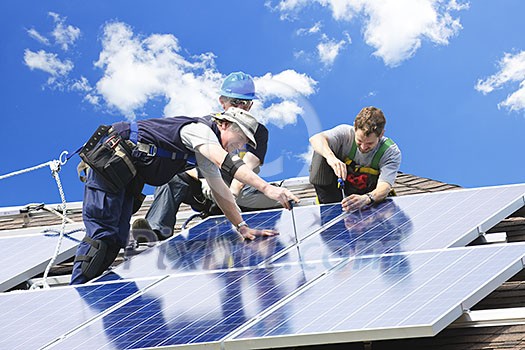 Workers installing alternative energy photovoltaic solar panels on roof