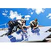 Workers installing alternative energy photovoltaic solar panels on roof