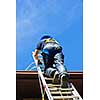 Construction worker climbing extension ladder to roof