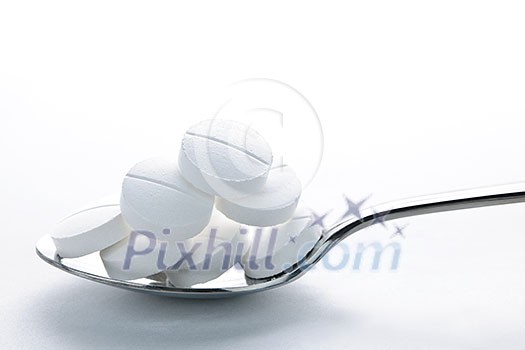 Calcium supplement pills piled on metal spoon closeup