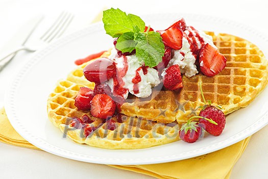 Plate of belgian waffles with fresh strawberries and whipped cream