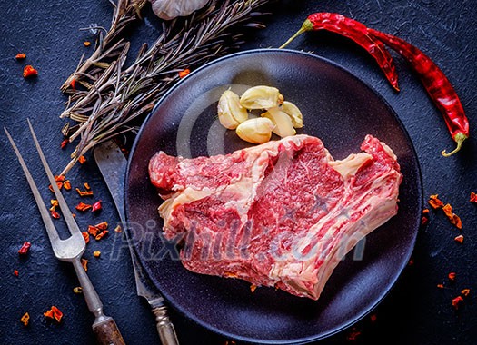 Raw meat steak entrecote on the plate with spice on the dark table