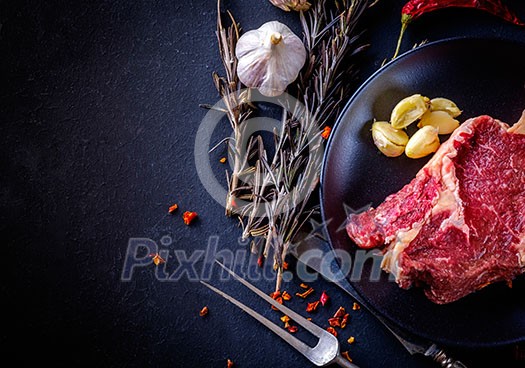 Raw meat steak entrecote on the plate with spice on the dark table