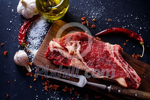 Raw meat steak entrecote on the cutting board with spice on the dark table. Raw meat steak entrecote on the cutting board with spice on the dark table.