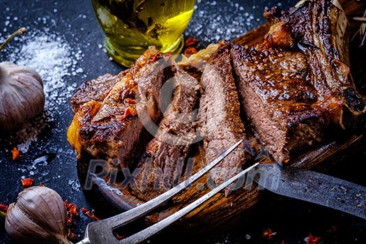 Grilled steak sliced on a cutting board. Entrecote with garlic and chilli on a dark background.