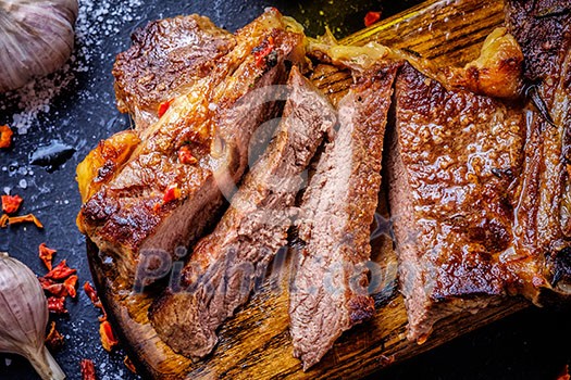 Grilled steak sliced on a cutting board. Entrecote with garlic and chilli on a dark background.