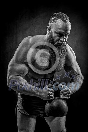 Bodybuilder with a beard lifts a heavy kettlebell. Black and white portrait of a strongman. Bodybuilder with a beard lifts a heavy kettlebell. Black and white portrait of a strongman.