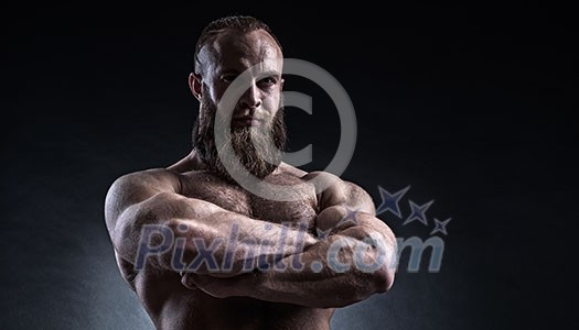 Strong bearded man with perfect abs, shoulders, biceps, triceps and chest. Bodybuilder topless over black background.