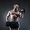 Power athletic bearded man in training pumping up muscles with dumbbell. Strong bodybuilder with six pack, perfect abs, shoulders, biceps, triceps and chest. 