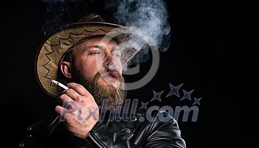 Man Smokes a cigarette. Man in cowboy hat with a cigarette in his hand over black background. Man Smokes a cigarette. Man in cowboy hat with a cigarette in his hand over black background.