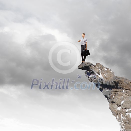 Risky businesswoman standing on edge of rock Risky businesswoman standing on edge of rock