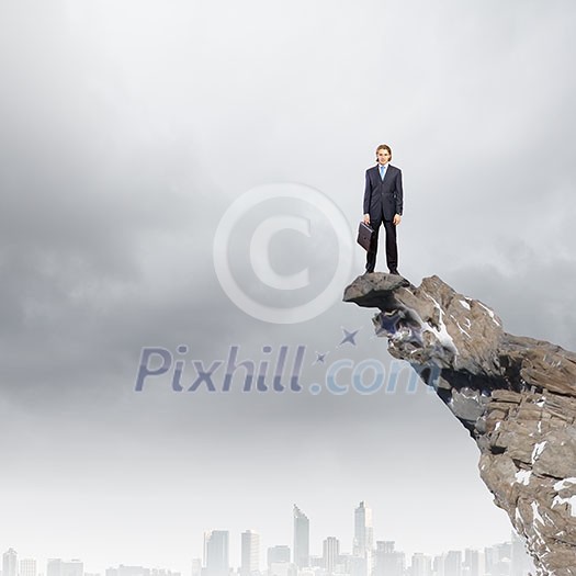 Young businessman standing on edge of rock mountain Young businessman standing on edge of rock mountain