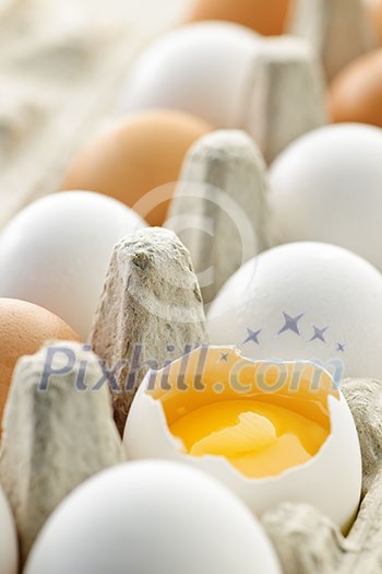 White and brown eggs in carton with broken egg