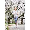 Beautiful teenage girl jogging in park with blooming apple trees