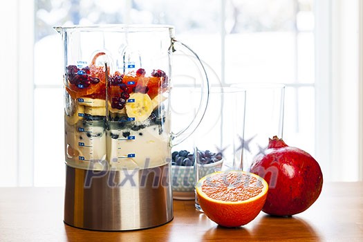 Healthy smoothie ingredients in blender with fresh fruit ready to blend on kitchen table