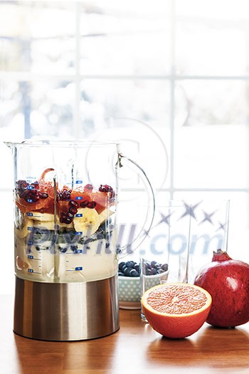 Healthy smoothie ingredients in blender with fresh fruit ready to blend on kitchen table