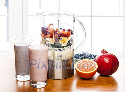 Prepared smoothies and healthy smoothie ingredients in blender with fresh fruit ready to blend on kitchen table