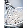Closeup of metal whisk whipping cream in glass bowl