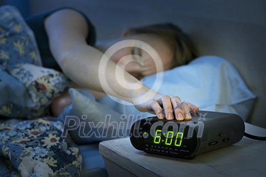 Young woman pressing snooze button on early morning digital alarm clock radio