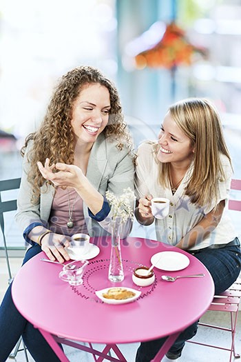 Two smiling women meeting for coffee in cafe and laughing