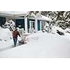Man using snowblower to clear deep snow on driveway near residential house after heavy snowfall