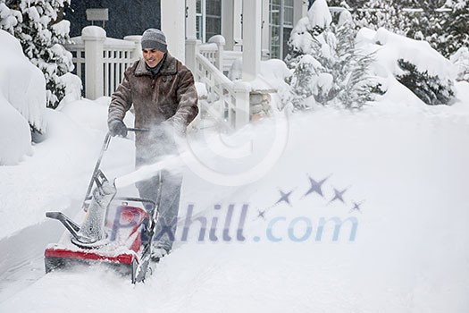 Man using snowblower to clear deep snow on driveway near residential house after heavy snowfall. Man using snowblower to clear deep snow on driveway near residential house after heavy snowfall.