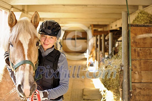 Young female rider with horse inside stable