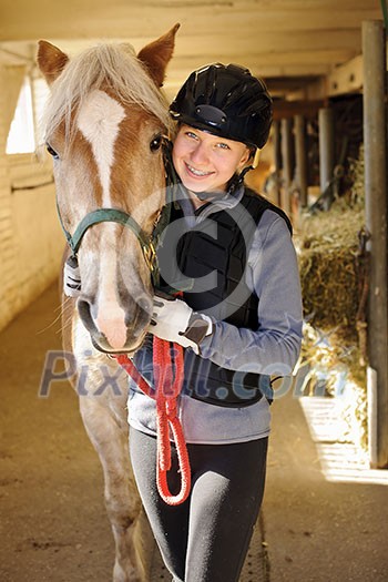 Young female rider with horse inside stable