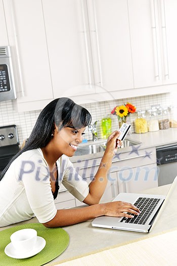 Smiling black woman online shopping using computer and credit card in kitchen Smiling black woman online shopping using computer and credit card in kitchen