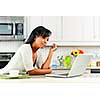 Thoughtful black woman using computer in modern kitchen interior