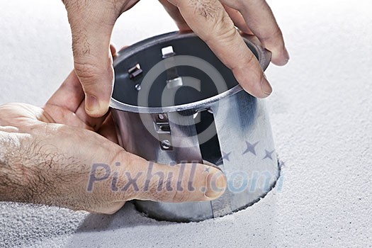 Hands installing round metal pot light fixture into ceiling tile Hands installing round metal pot light fixture into ceiling tile