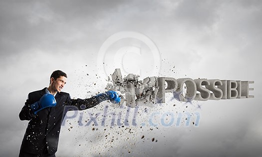 Young businessman in blue boxing gloves breaking impossible word Young businessman in blue boxing gloves breaking impossible word