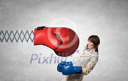 Young businesswoman in blue boxing gloves fighting big red glove on spring