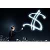 Businesswoman in darkness drawing dollar sign with flashlight