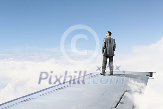 Young businessman standing on edge of airplane wing Young businessman standing on edge of airplane wing