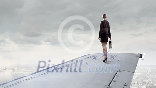 Young businesswoman standing on edge of airplane wing