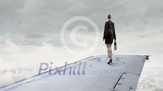 Young businesswoman standing on edge of airplane wing Young businesswoman standing on edge of airplane wing
