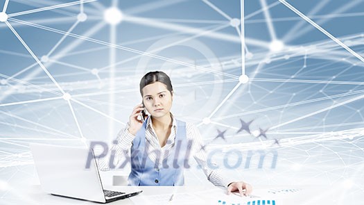 Beautiful young lady at desk talking on mobile phone with social network concept at background