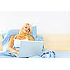 Happy blonde woman using computer at home sitting in bed