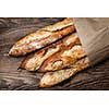 Four baguette bread loaves in paper bag on wooden background