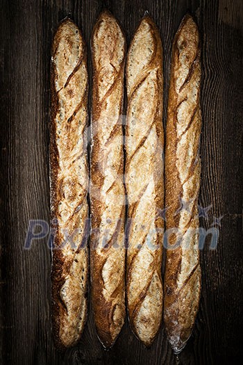 Four whole baguette bread loaves on dark wooden background Four whole baguette bread loaves on dark wooden background