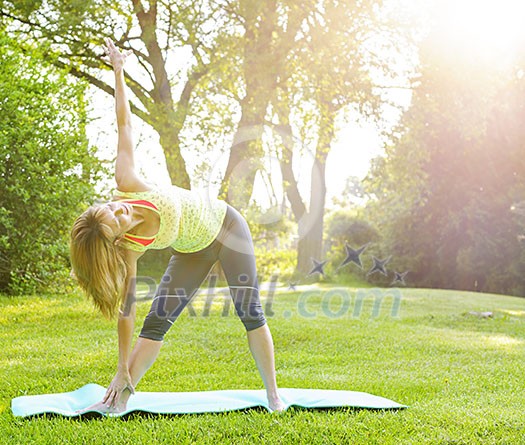 Female fitness instructor doing yoga extended triangle pose outdoors in morning sunshine