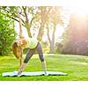 Female fitness instructor doing yoga extended triangle pose outdoors in morning sunshine