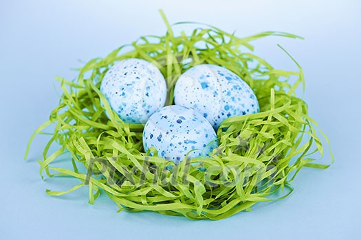 Three blue speckled easter eggs in green paper grass nest
