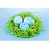 Three blue speckled easter eggs in green paper grass nest