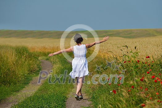 Young woman standing jumping and running  on a wheat field with blue sky in  background at summer day representing healthy life and agriculture concept